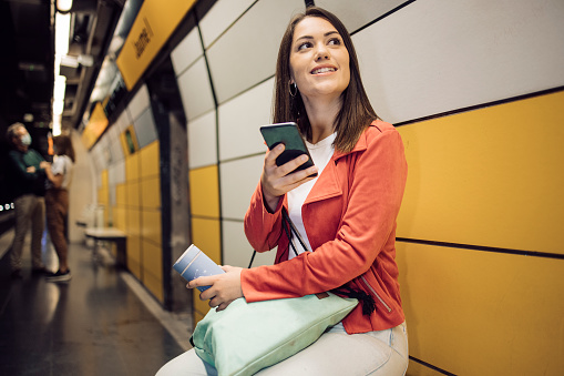 Portrait of a young woman on vacation in Barcelona waiting for his train in the subway and using his smartphone.