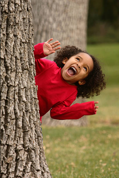 A happy child in red jacket is peaking from behind a tree stock photo