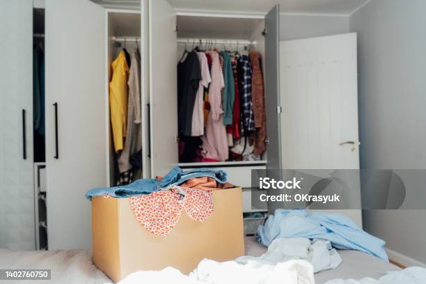 A Cardboard Box Of Selected Clothes For Donating To A Charity Shop Standing On The Bed Decluttering Sorting Clothes And Cleaning Up Reuse Secondhand Conscious Consumer Sustainability Stock Photo - Download Image Now