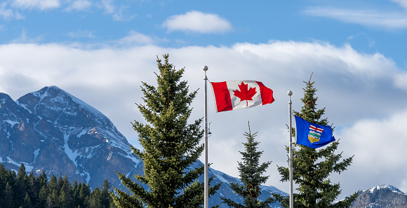 National Flag of Canada and Flag of Alberta. Natural mountains and trees scenery in the background.