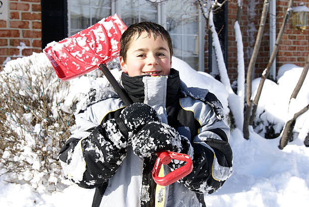Young boy holding a red snow shovel.