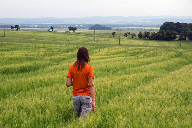 Photo girl in orange shirt walking in green wheat field looking out over wide valley