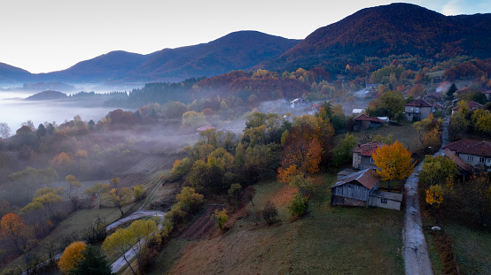Mountain landscape with houses and a road in fog over a small village through the autumn, drone view