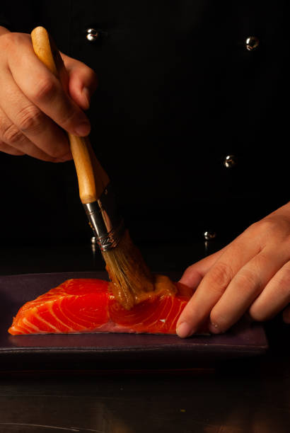 Chef's hand brushing a salmon . - stock photo