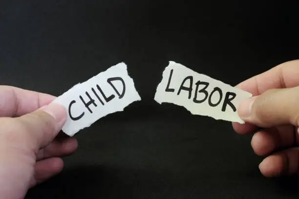 Photo of Stop and fight child labor concept. Human hand tearing a piece paper with written word child labor. Children rights protection.