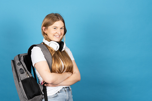 Portrait of blonde student with long hair and wearing backpack isolated on blue background.