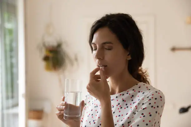 Stressed tired woman taking vitamins, painkillers, antidepressants, pills, meds against headache, insomnia, nervous disorder, anxiety. Patient with medication fighting against flu infection, migraine