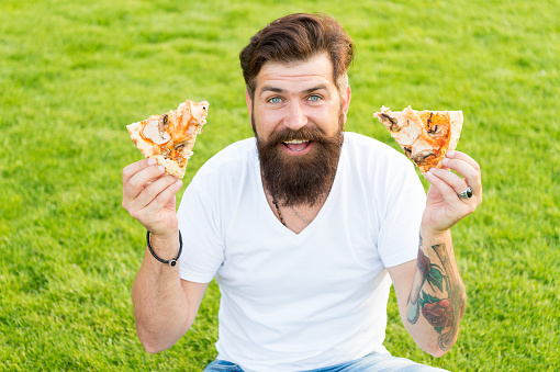 Both pieces for me. Man bearded hipster eating delicious pizza. Cheerful guy eat pizza. Summer picnic concept. Caucasian male loving Italian traditional food. Hungry greedy man hold pizza in hands.