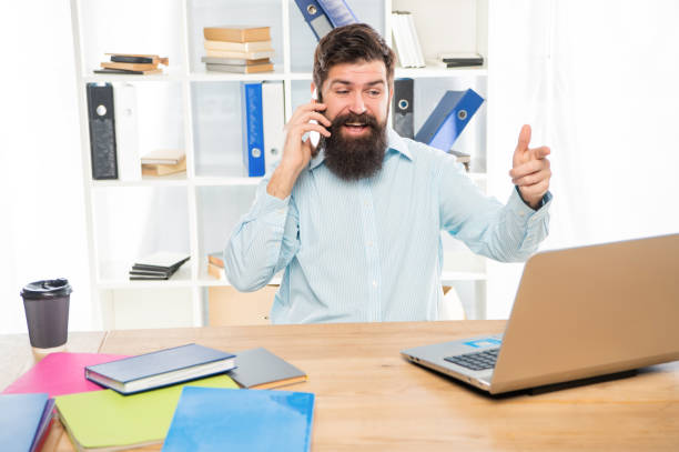 istock Happy guy talking on mobile phone working on laptop in office, business call 1402809491