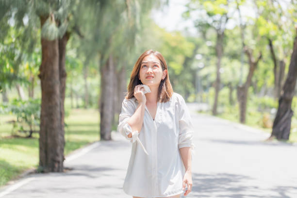 donna che cammina nel parco avendo colpo di sole in estate tempo caldo, giovane ragazza graziosa che asciuga il sudore usando una salvietta in una calda giornata estiva in un parco - heat female summer vacations foto e immagini stock