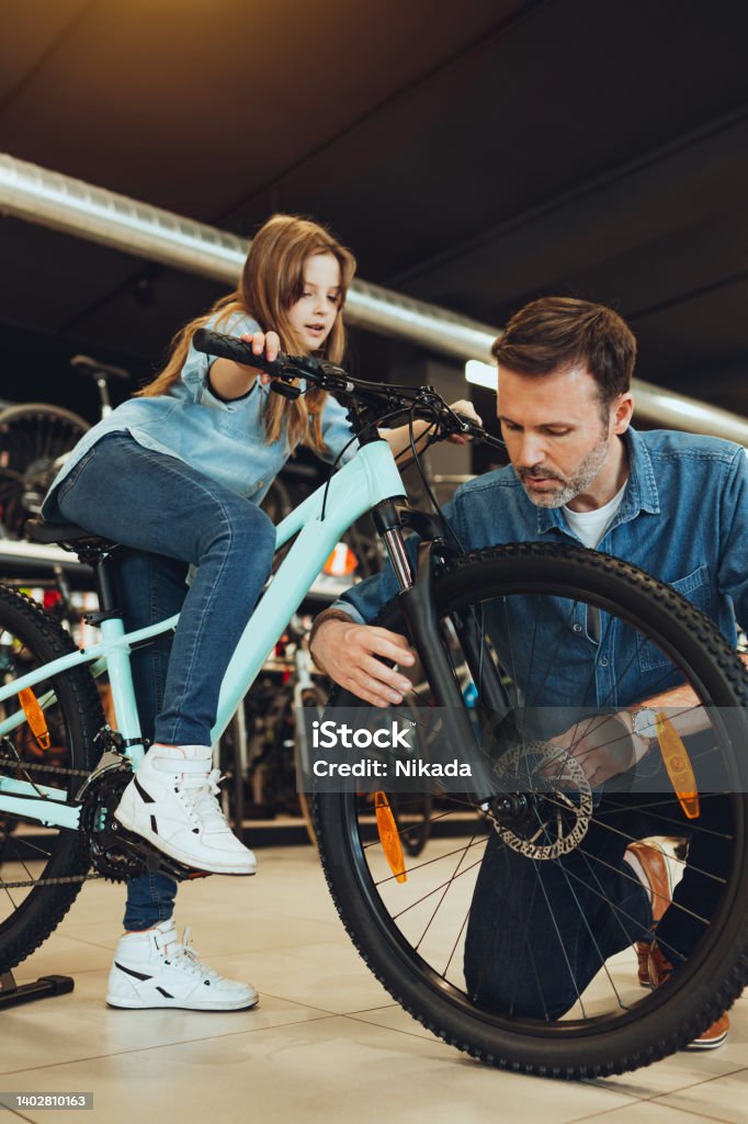 man and his daughter testing bicycles in bike shop man and his daughter checking out bicycles in bike shop Bicycle Shop Stock Photo