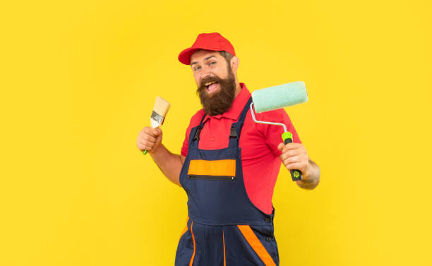 istock happy man in work clothes hold paint roller and brush on yellow background 1402811414