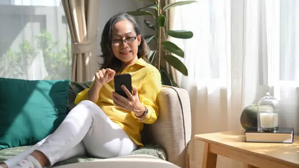 Photo of Smiling mature woman chatting with relatives online, shopping, checking social media on smart phone.