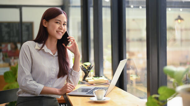 istock Gorgeous asian business woman having cell phone conversation while sitting front open laptop computer in coffee shop. 1402814348