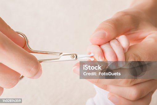 istock Young adult mother hands cutting newborn finger nails with scissors. Closeup. 1402814359