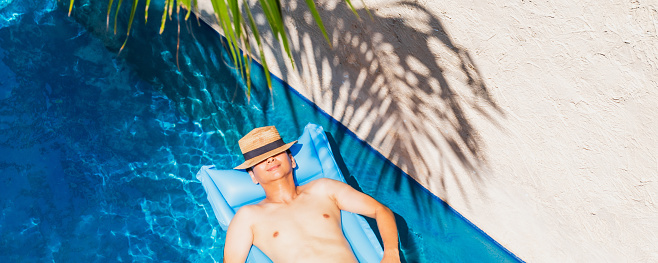 Asian traveler man sleep on pool float air mat in the swimming pool in tropical resort hotel background.Concept of a happy summer holiday travel.