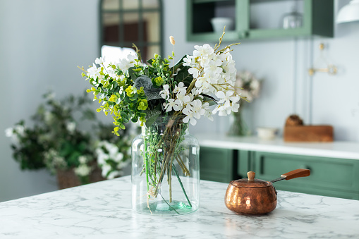 Summer white flowers and turk with coffee in kitchen table. Bouquet of flowers and plants in glass vase at home. Greeting card. Home interior with cozy Scandinavian decor. Utensil on dining table