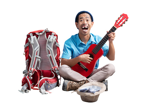 Asian man with a beanie hat and a backpack playing guitar to make money isolated over white background