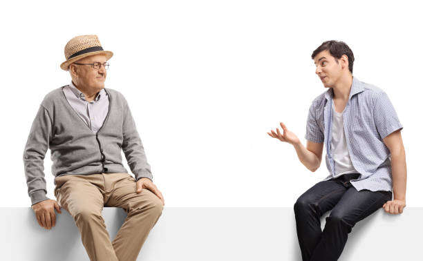 istock Elderly man and a guy talking and sitting on a blank panel 1402827031