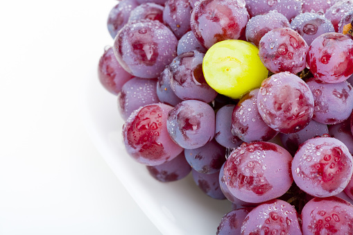 Fresh group of wet and clean purple grapes with a single green grape on white plate