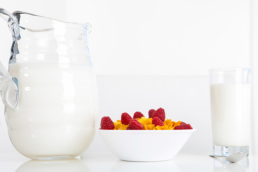 Morning Cornflakes cereal bowl with raspberry topping with glass of milk on dining room table