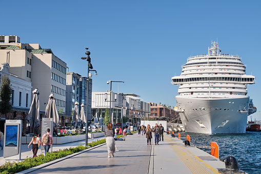 Istanbul, Turkey - May 9, 2022: People walking by the sea in Galataport, huge cruise ship can be seen on the right side. Galataport is a cruise ship port and mixed-use property in Karakoy district.