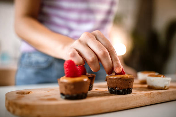 Mid adult woman making small cheesecake bites in home kitchen. Decorating it with raspberries