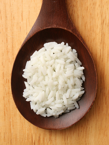 Top view of wooden spoon with boiled white rice on it