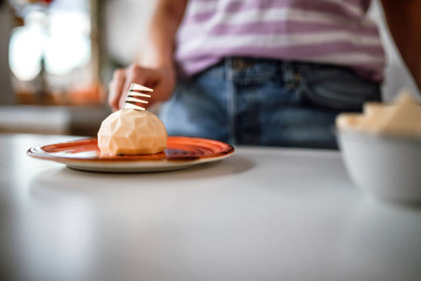 Woman tasting delicious chocolate cake with fork, on orange plate on dining table.
