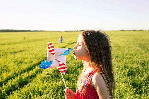 US Independence Day. patriotic background with kids. child girl blows on pinwheel in field in nature in summer outdoor. kids fun.