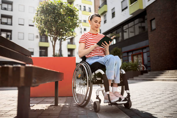 joven sonriente en silla de ruedas leyendo libro - outdoors book reading accessibility fotografías e imágenes de stock