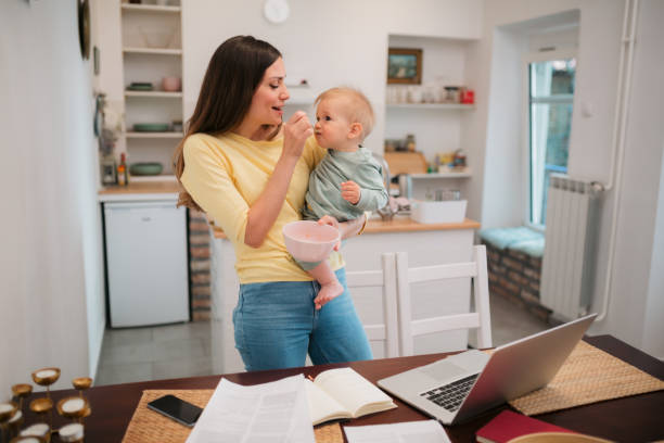 Young adult mother trying to work from home while holding her baby stock photo