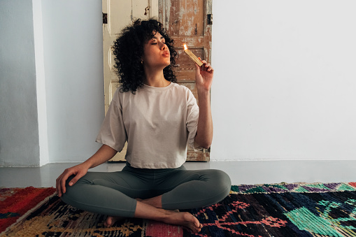 Young multiracial woman blowing flame of palo santo stick preparing to meditate. Copy space. Meditation and spirituality concept.