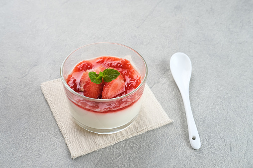 Sweet vanilla silky pudding dessert with strawberry sauce, sliced ​​fresh strawberries and mint on a glass