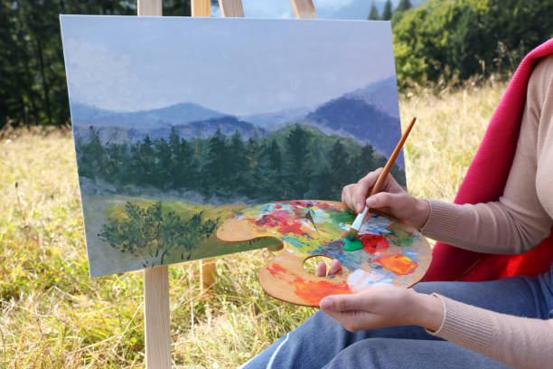 istock Young woman drawing on easel with brush outdoors, closeup 1402841042