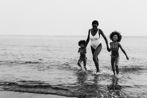 African sisters twins running on the beach with smiling mother - Focus on right girl face - Black and white editing