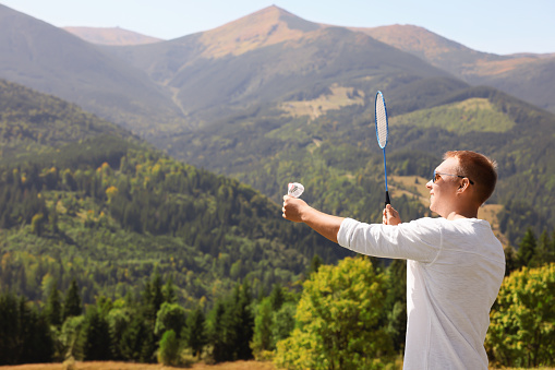 Man playing badminton in mountains on sunny day. Space for text