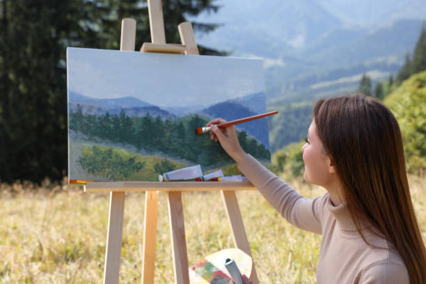 istock Young woman drawing on easel in mountains 1402841392