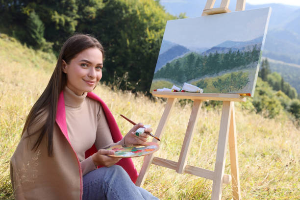 istock Young woman drawing on easel in mountains 1402841423