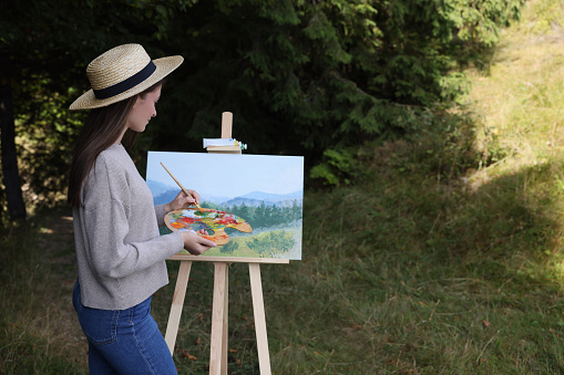 Young woman drawing on easel outdoors, space for text