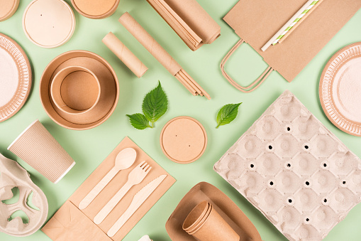 Flat lay with eco tableware, paper utensils and wooden bamboo cutlery set over light green background. Sustainable food packaging concept