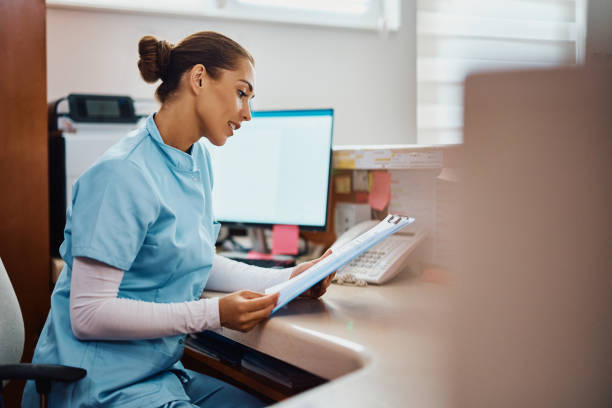 young nurse going through medical records at reception desk in the hospital. - recepção imagens e fotografias de stock