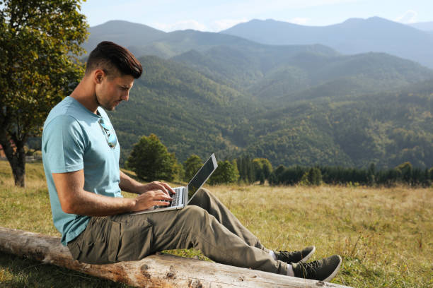 istock Man working with laptop in mountains on sunny day 1402842061