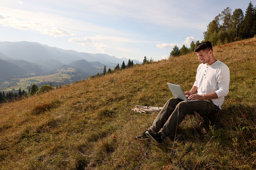 Man working with laptop outdoors surrounded by beautiful nature. Space for text