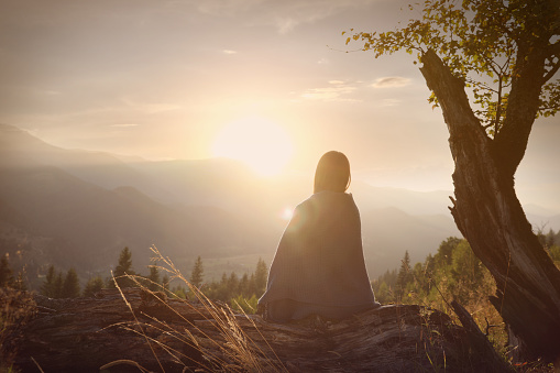 Woman with cozy plaid enjoying sunset in mountains, back view