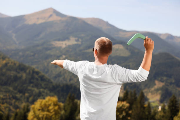 man throwing boomerang in mountains on sunny day, back view - boomerang imagens e fotografias de stock