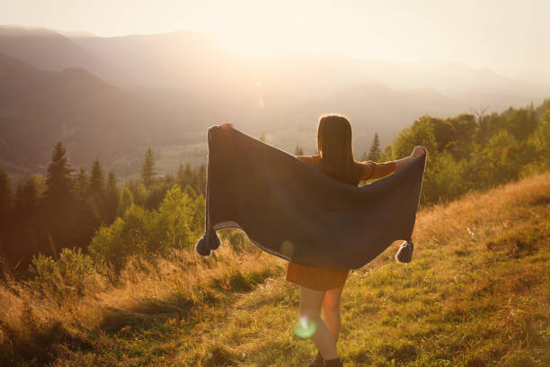 istock Woman with cozy plaid enjoying warm sunlight in mountains, back view 1402843700