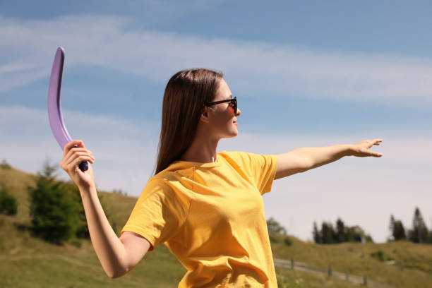 Young woman throwing boomerang outdoors on sunny day Young woman throwing boomerang outdoors on sunny day airfoil photos stock pictures, royalty-free photos & images