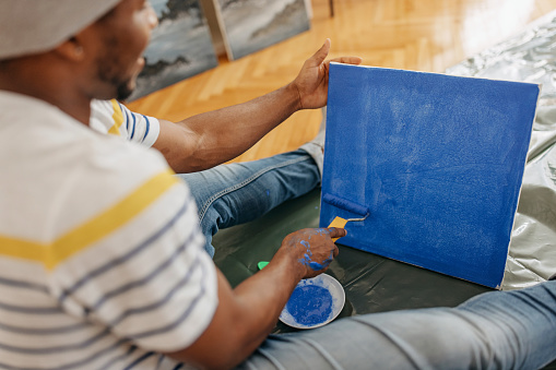Black man sitting on the living room floor and painting his canvas