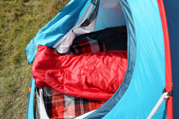 istock Red sleeping bag in camping tent on green grass outdoors, above view 1402845000